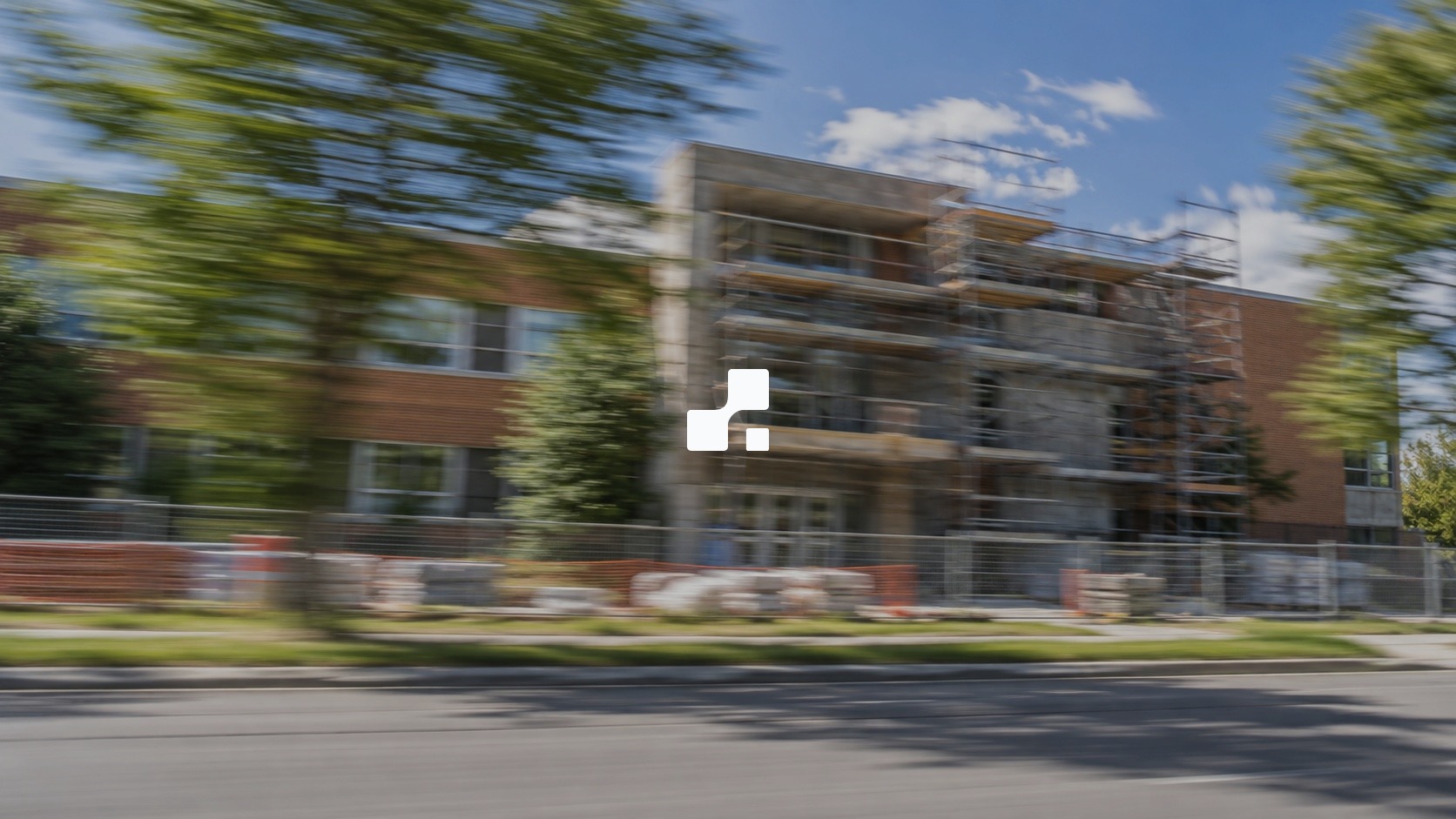 Summer view of a brick institutional building under renovation, blurred by lateral camera movement, with the Aplon mark